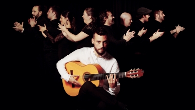 Daniel Martinez sits playing a guitar against a black background. 